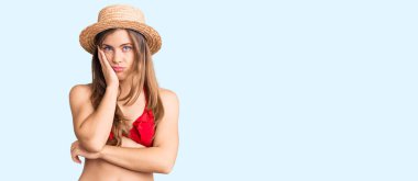 Bikini ve yaz şapkası takan güzel beyaz kadın kollarını kavuşturarak depresyondan sıkılmış ve yorgun görünüyor.. 