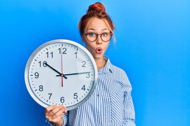 Genç kızıl saçlı kadın büyük saati tutuyor. Korkmuş ve şaşkın bir şekilde ağzı açık, şaşırmış, inançsız bir yüz. 