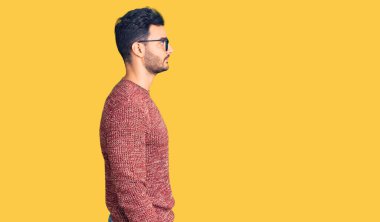 Kışlık süveter ve gözlük takan genç yakışıklı İspanyol adam yan yan yan bakıyor, rahat poz veriyor kendine güvenen bir gülümsemeyle doğal bir yüz.. 