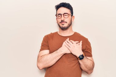 Gündelik kıyafetler giyen genç İspanyol adam elleri göğsünde gülümsüyor, gözleri kapalı ve yüzünde minnet ifadesi var. sağlık kavramı. 