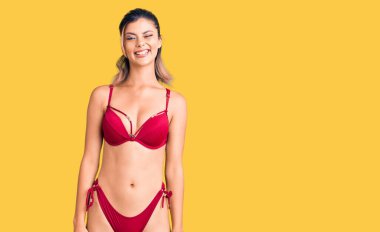 Bikini giyen genç güzel bir kadın kameraya seksi bir ifadeyle bakıyor, neşeli ve mutlu bir yüzle.. 