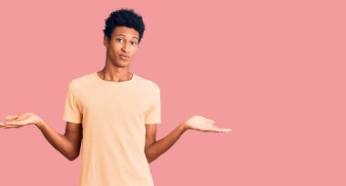 Sıradan kıyafetler giyen, kafası karışmış, elleri ve kolları havada genç Afro-Amerikalı bir adam. şüphe kavramı. 