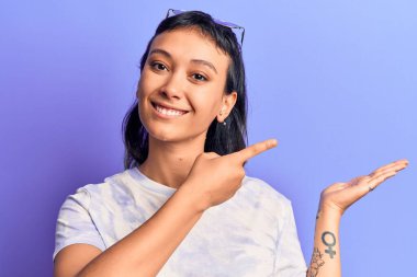 Gündelik giysiler giyen genç bir kadın kameraya hayret eder ve gülümserken elini ve parmağını gösterir.. 