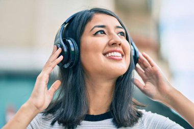Genç İspanyol kadın gülümseyerek şehirde kulaklık takarak müzik dinliyor..