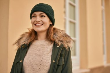 Genç beyaz kız gülümseyerek şehirde mutlu mesut duruyor..