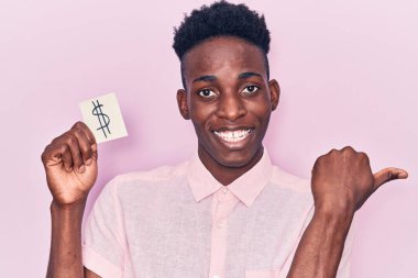 Elinde dolar sembolü olan genç Afro-Amerikan bir adam başparmağıyla işaret ederek ağzı açık gülümsüyor. 