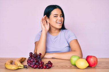 Genç ve güzel Asyalı kız taze ve sağlıklı meyve yiyor. Kulaktan kulağa gülümsüyor ve söylenti ya da dedikoduları dinliyor. Sağırlık kavramı. 