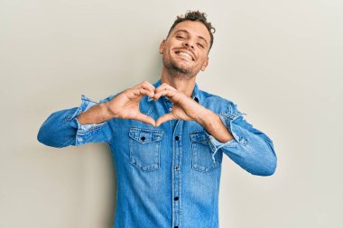 Gündelik kıyafetler giyen, aşık gülümseyen, elleriyle kalp sembolü yapan genç bir İspanyol. romantik kavram. 