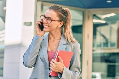 Genç sarışın iş kadını gülümsüyor. Şehirdeki akıllı telefondan konuşuyor..