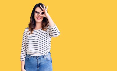 Güzel, genç, esmer bir kadın günlük kıyafetler ve gözlük takıyor. El hareketleriyle gülümsüyor, gözleriyle mutlu yüzüyle parmaklarının arasından bakıyor.. 