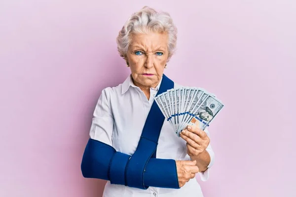Starsza Siwowłosa Kobieta Ramionach Temblaku Trzymająca Banknoty Dolarowe Usa Sceptyczna — Zdjęcie stockowe