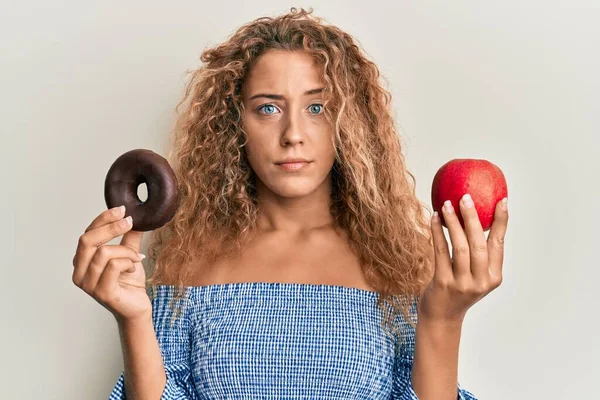 漂亮的高加索少女拿着红苹果和甜甜圈的怀疑和紧张 皱着眉头因问题而烦恼 消极的人 — 图库照片
