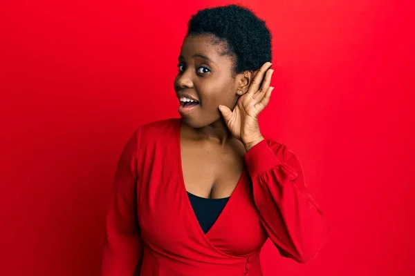 年轻的非洲女人 有着一头黑发 身穿红色背景的休闲服 双手相对地微笑 聆听流言或流言蜚语 聋的概念 — 图库照片