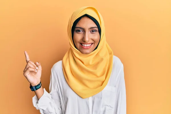 若いですブルネットArab女性身に着けています伝統的なイスラムヒジャーブスカーフで顔に大きな笑顔 カメラを見て側に手指で指して — ストック写真