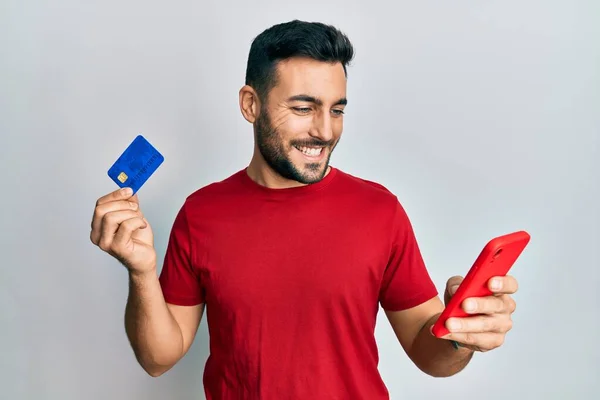 Joven Hombre Hispano Sosteniendo Teléfono Inteligente Tarjeta Crédito Sonriendo Con —  Fotos de Stock