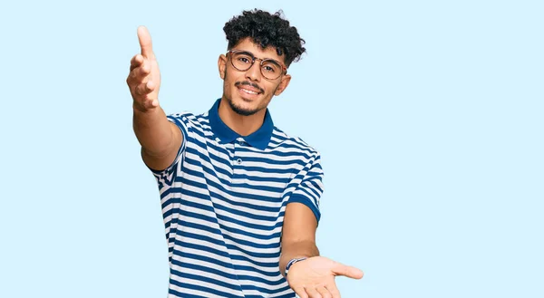 年轻的阿拉伯男子身穿休闲装 戴着眼镜 看着镜头 张开双臂拥抱 欢快的表达拥抱幸福 — 图库照片