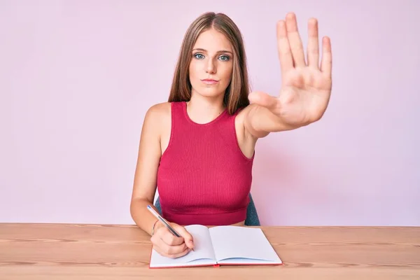 Jovem Caucasiana Escrevendo Caderno Sentado Mesa Com Mão Aberta Fazendo — Fotografia de Stock