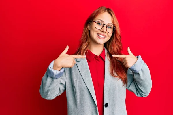 年轻的红头发女人穿着商务外套 戴着眼镜 脸上挂着微笑 用手指指着自己 自豪而快乐 — 图库照片