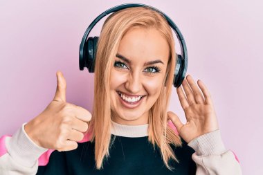 Güzel, beyaz bir kadın müzik dinliyor, kulaklık takıyor, gülümsüyor, gülümsüyor ve olumlu bakıyor.   