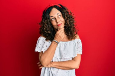 Orta yaşlı İspanyol kadın. Elleri çenesinde gündelik giysiler giyip soru soruyor. Düşünceli bir ifade. Düşünceli bir yüzle gülümsüyor. şüphe kavramı. 