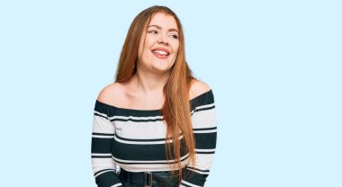 Güzel, kızıl saçlı, zarif kıyafetler giyen, yüzünde gülümseme, doğal bir ifade olan genç bir kadın. Kendinden emin gülen. 