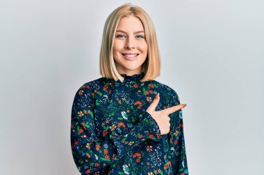 Yüzünde mutlu ve doğal bir ifade olan, elleri ve parmaklarıyla işaret eden, güler yüzlü, gündelik kıyafetler giyen genç sarışın kadın. 