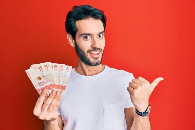 Genç İspanyol adam elinde 10 Kolombiya pezosu ile baş parmağını kaldırıyor ve ağzı açık gülümsüyor. 