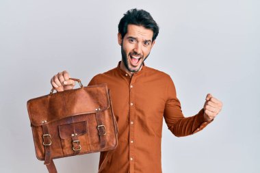 Deri çanta giyen İspanyol genç adam gururla bağırıyor, zaferi kutluyor ve başarıyı kollarını kaldırarak kutluyor. 