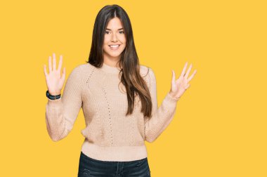 Kış süveteri giyen genç esmer kadın dokuz numarayı gösterip işaret ederken kendine güvenen ve mutlu bir şekilde gülümsüyor.. 