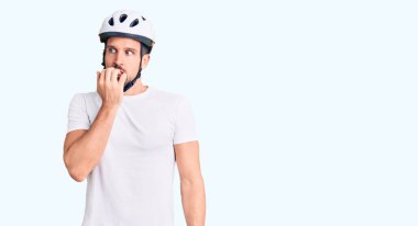 Bisiklet kaskı takan yakışıklı bir genç stresli ve gergin görünüyor. Elleri ağızdan tırnak yiyor. anksiyete. 