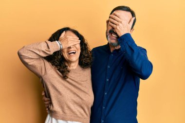 Orta yaşlı İspanyol çift, sıradan kıyafetler giyip, gülümsüyor ve elleri yüzlerinde, şaşkınlıktan gözleri kapayarak gülüyorlar. kör kavram. 