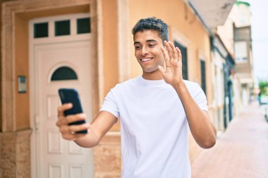 Genç Latin adam gülümseyerek şehirde akıllı telefon kullanarak video araması yapıyor..