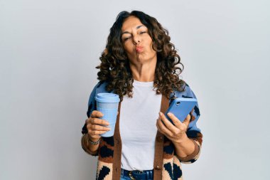 Orta yaşlı İspanyol bir kadın bir fincan kahve içiyor ve akıllı telefon ekranına bakıyor. Öpücük üflerken kameraya bakıyor. Sevimli ve seksi. aşk ifadesi. 