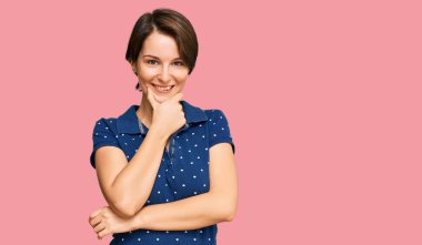 Kısa saçlı, kısa saçlı, rahat giyinen, kameraya kendinden emin, kolları çapraz ve çenesi açık gülümseyen genç esmer kadın. Olumlu düşünmek. 