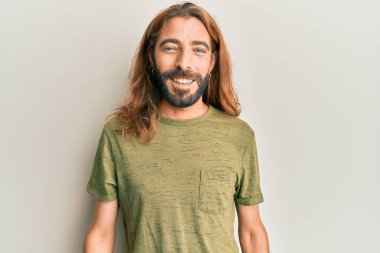 Uzun saçlı, sakallı, sıradan kıyafetler giyen, mutlu ve havalı bir gülümsemesi olan çekici bir adam. şanslı kişi. 