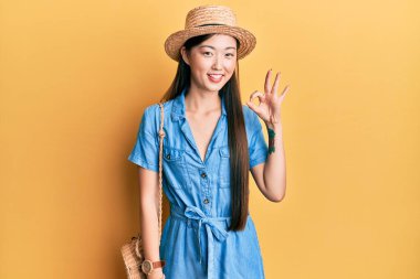 Yazlık şapkalı genç Çinli kadın olumlu gülümsüyor. El ve parmaklarıyla tamam işareti yapıyor. başarılı ifade. 