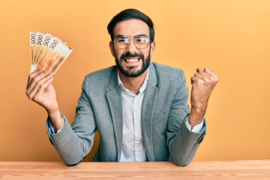 Genç İspanyol adam elinde Norveç kronu banknotları tutarak masaya oturmuş gururla bağırıyor, zaferi ve başarıyı kutluyor. 