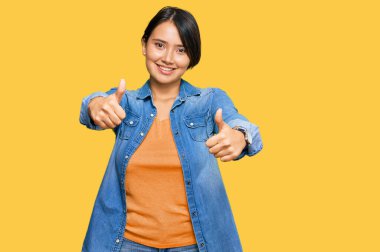 Kısa saçlı, kısa saçlı, genç, İspanyol bir kadın. Sıradan bir kot ceket giyiyor. Elleriyle olumlu bir jest yapıyor. kazanan jest. 