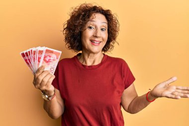 Güzel, orta yaşlı olgun bir kadın elinde 20 İsrail şekeri banknotlarıyla başarıyı mutlu bir gülümsemeyle ve kazanan ifadeyle kutluyor. 
