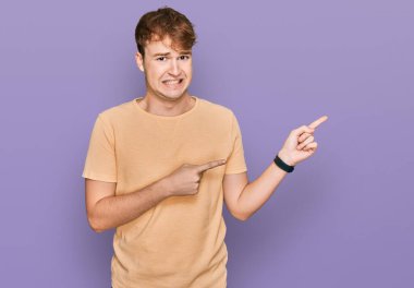 Gündelik giysiler giyen genç beyaz bir adam iki eliyle endişeli ve gergin bir ifadeye işaret ediyor. 