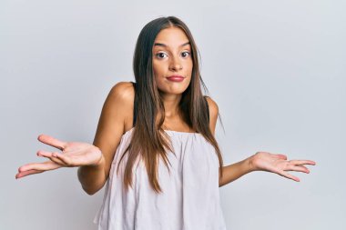 Gündelik kıyafetler giyen, elleri ve kolları havada, kafası karışmış genç İspanyol kadın. şüphe kavramı. 