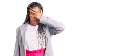 Saçları örgülü genç Afro-Amerikalı kadın şok içinde yüzünü ve gözlerini kapayarak utangaç ifadesiyle parmaklarından bakıyor.. 