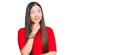 Elleri çenesinde gündelik giysiler giyen genç Çinli kadın soru sormayı düşünüyor, düşünceli bir ifade. Düşünceli bir yüzle gülümsüyor. şüphe kavramı. 