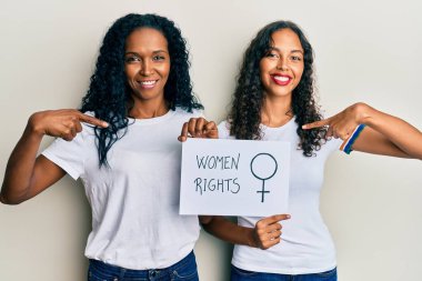 Afrika kökenli Amerikalı anne ve kız ellerinde kadın hakları afişi mutlu ve gururlu bir kendini işaret ediyor. 