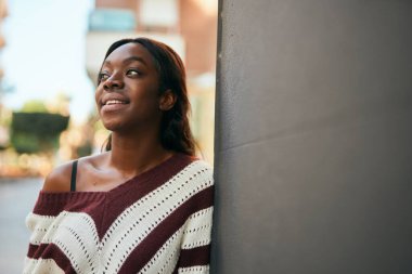 Genç Afrikalı Amerikalı kadın gülümseyerek şehirde mutlu mesut duruyor..
