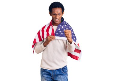 Amerika Birleşik Devletleri bayrağını tutan Afrikalı yakışıklı adam öfkeyle bağırıyor, öfkeyle bağırıyor ve el kaldırıyor. 