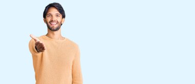 Yakışıklı İspanyol bir adam sıradan bir süveter giyip dostça el sıkışarak selam veriyor. başarılı iş. 