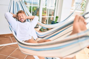 Yakışıklı beyaz adam mutlu bir şekilde gülerek terasta dinleniyor.