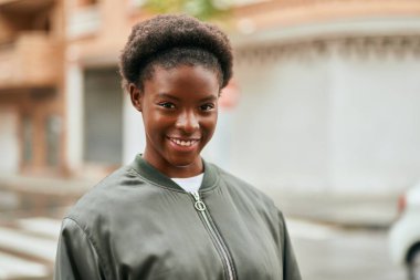 Genç Afrikalı Amerikalı kız gülümseyerek şehirde mutlu mesut duruyor..