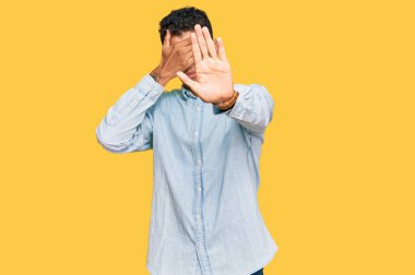 Genç, yakışıklı, Afro-Amerikan bir adam, günlük kıyafetler giyiyor, elleriyle gözleri örtüyor ve üzgün ve korku dolu ifadelerle jestleri durduruyor. utangaç ve olumsuz kavram. 